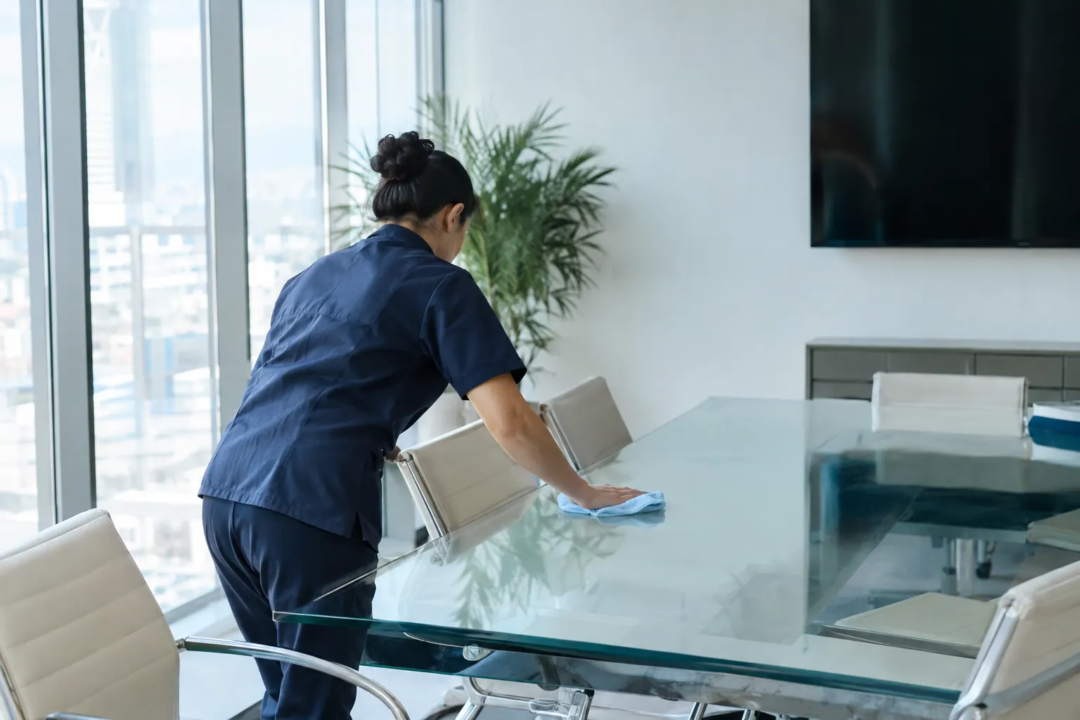 Reinigungskraft reinigt einen Glastisch in einem modernen Sitzungszimmer